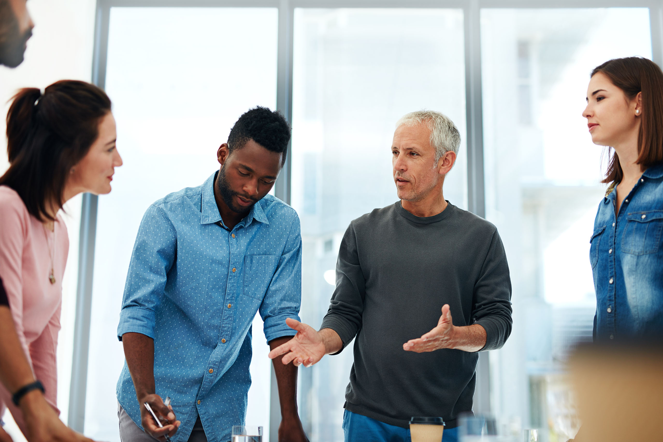 Businessman, coach and discussion with group in meeting for collaboration, creative planning or brainstorming at office. Man talking to team of employees in boardroom for idea in startup at workplace.