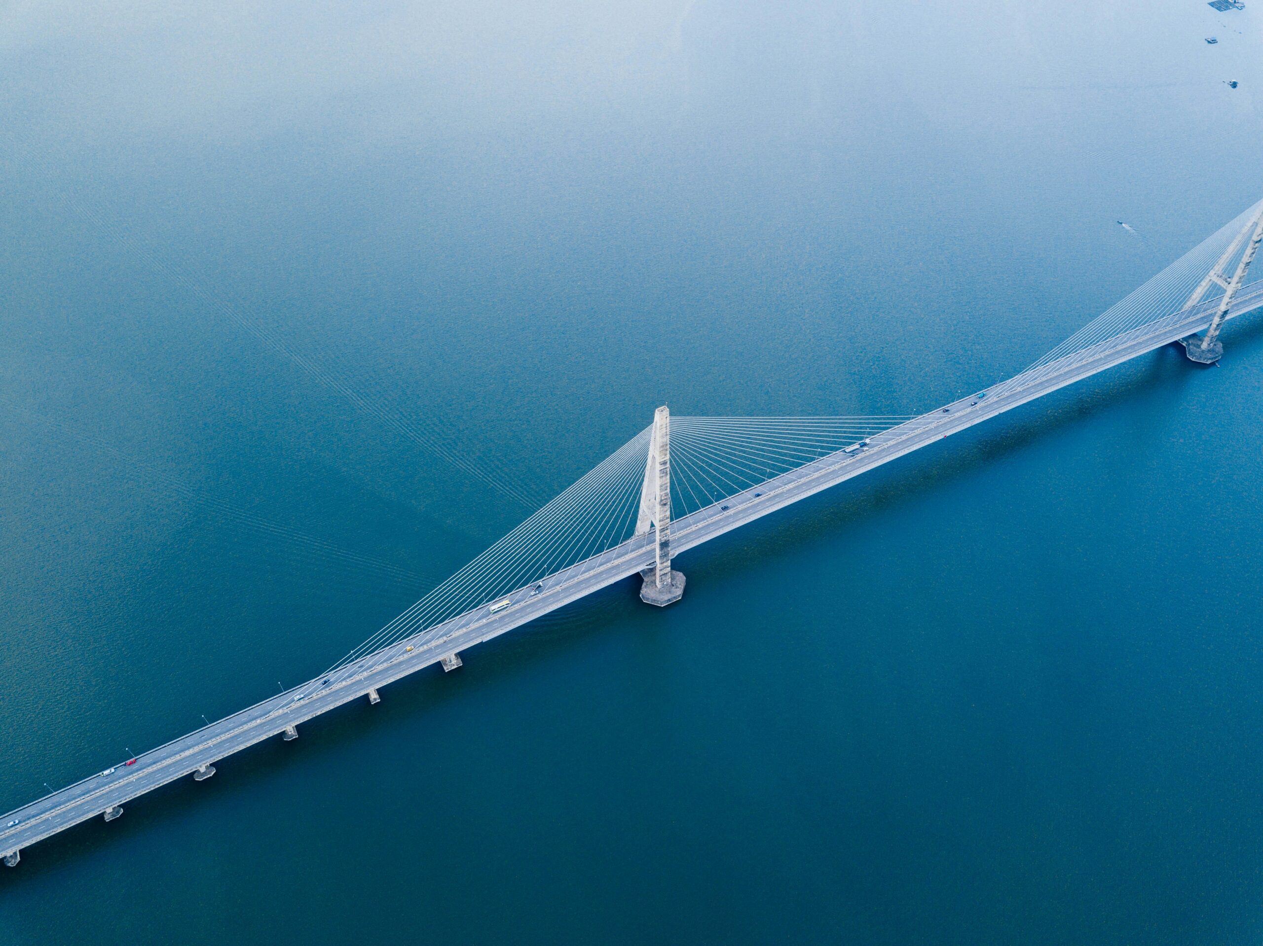 White bridge over the sea. There are cars driving on it.