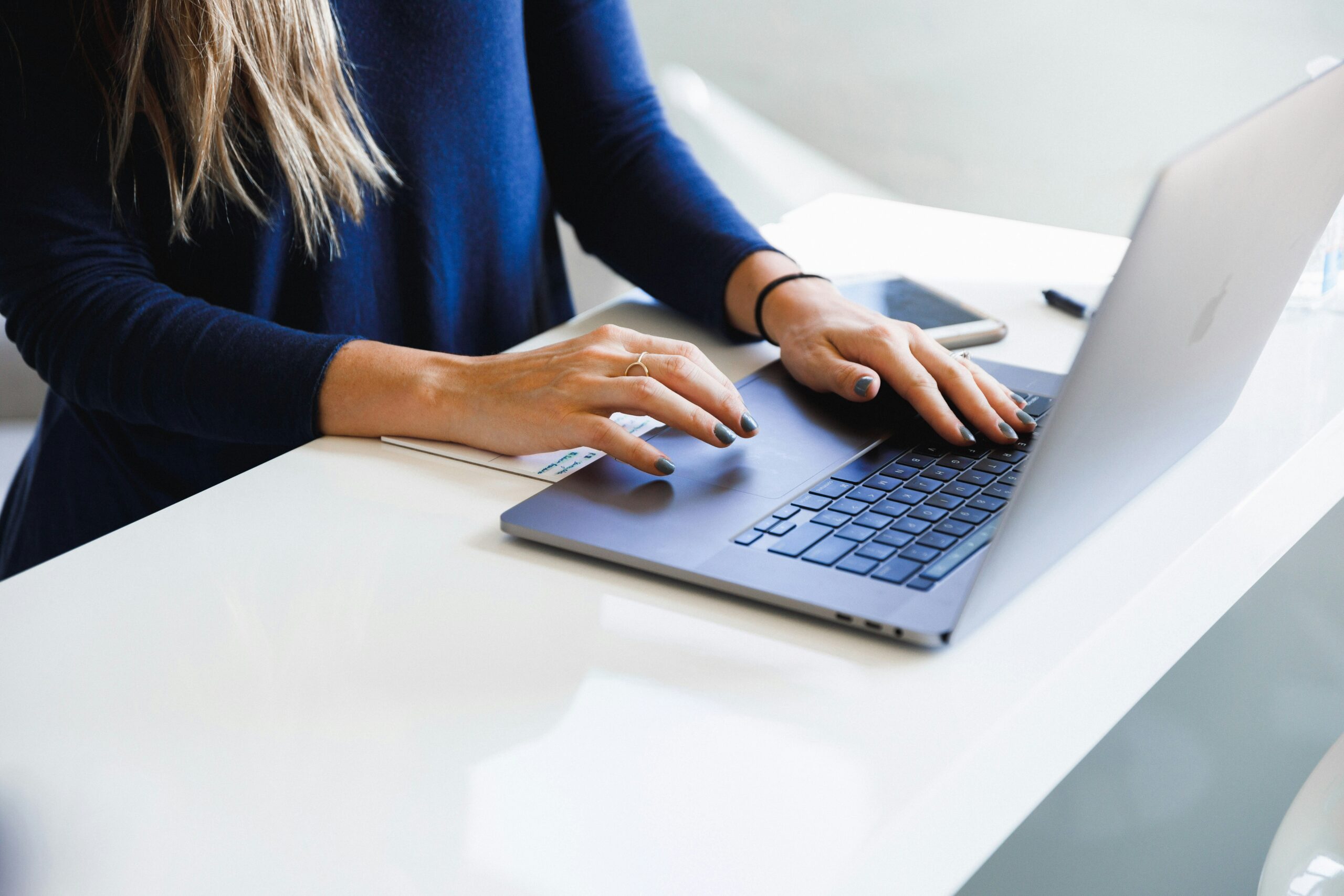 Woman standing at a desk typing on a laptop.
