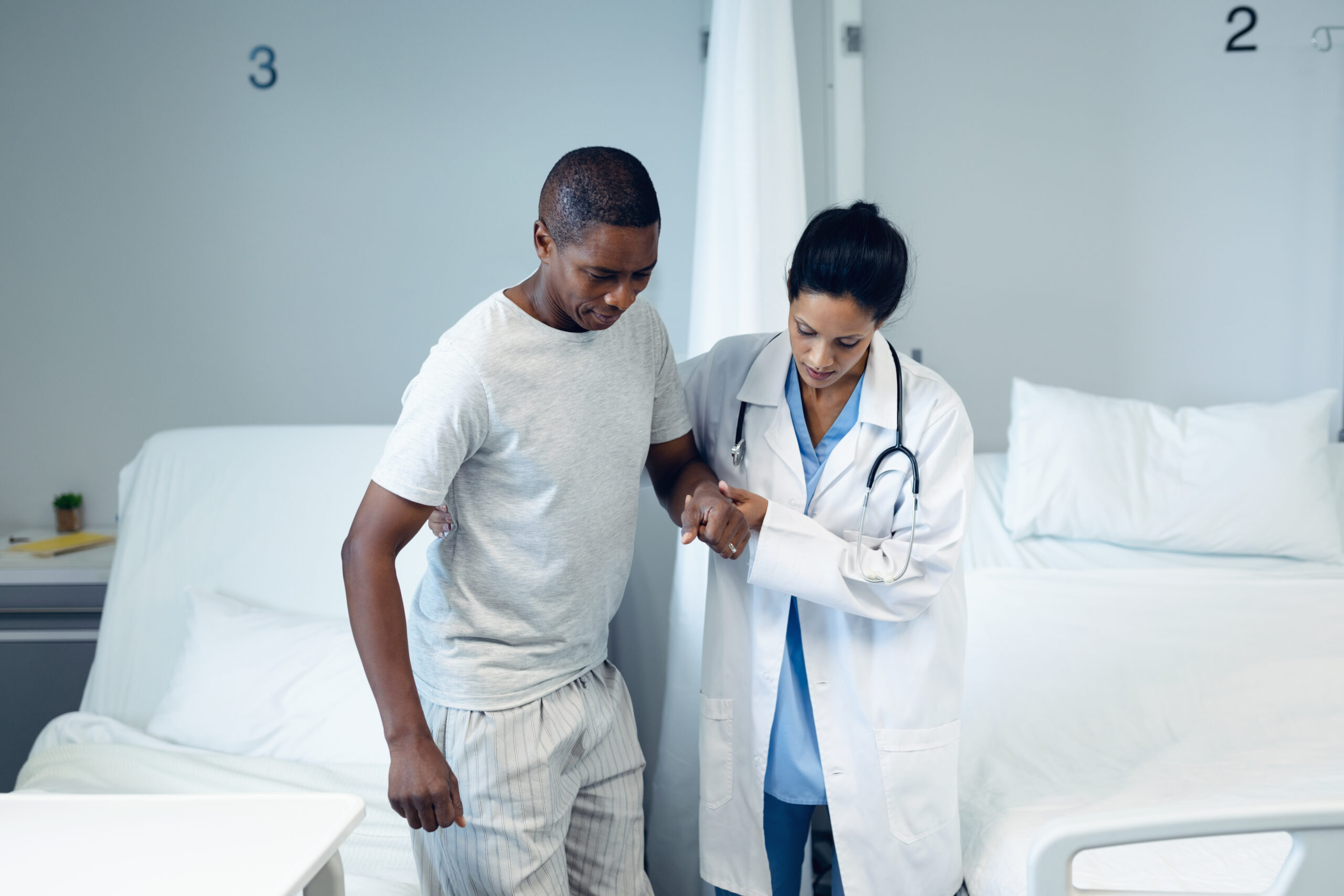 Female doctor helping male patient to walk in the ward